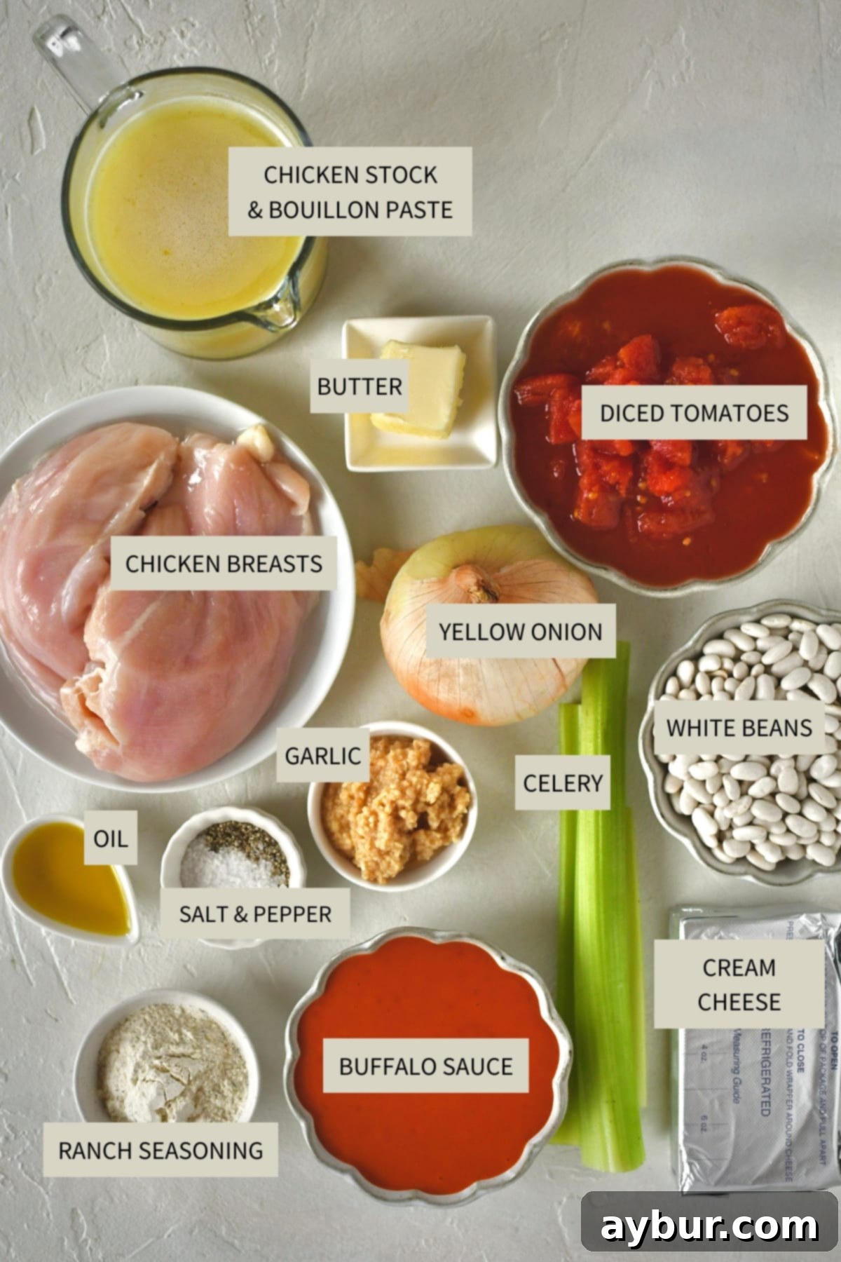 A carefully arranged spread of fresh ingredients required to prepare homemade Buffalo Chicken Chili, including chicken breasts, celery, onions, cans of beans, buffalo sauce, and various spices.