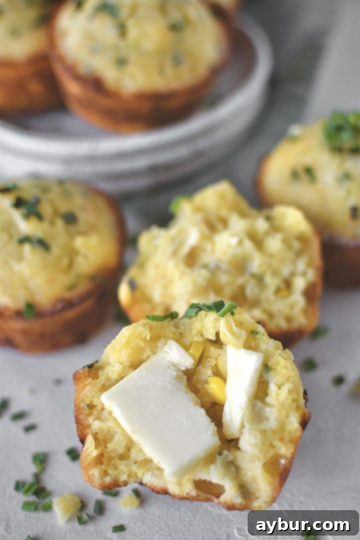 Cornbread Muffins scattered on counter, one split in half with butter on it.