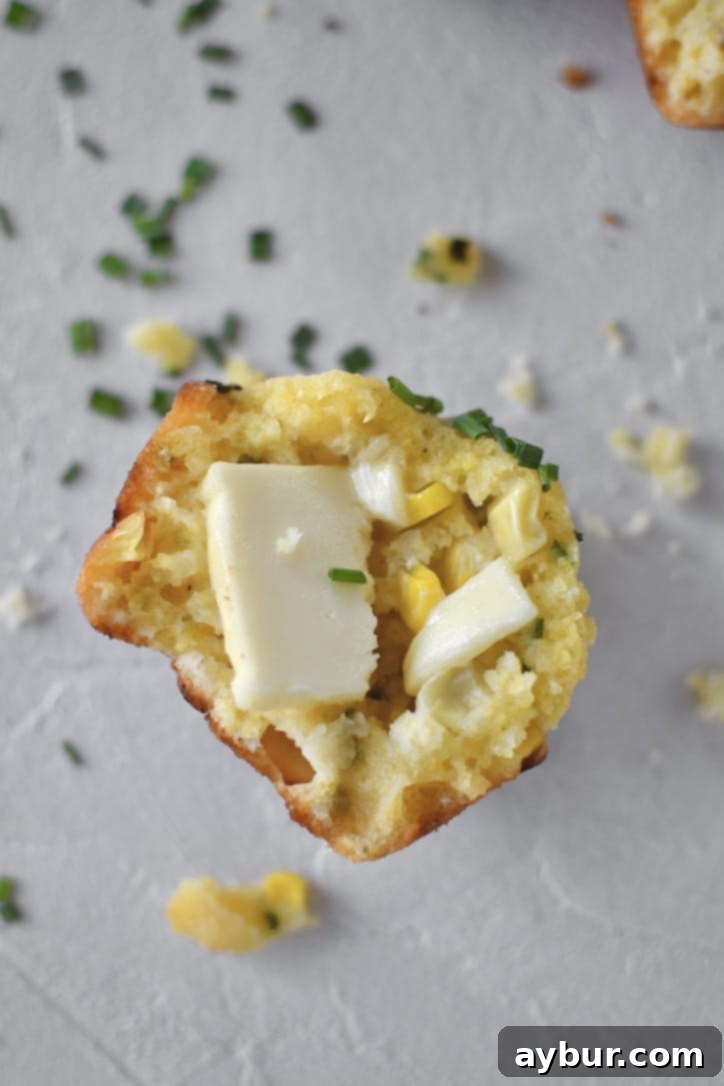 Half a Cornbread Muffin with crumbs all around it on a counter and butter on the muffin.