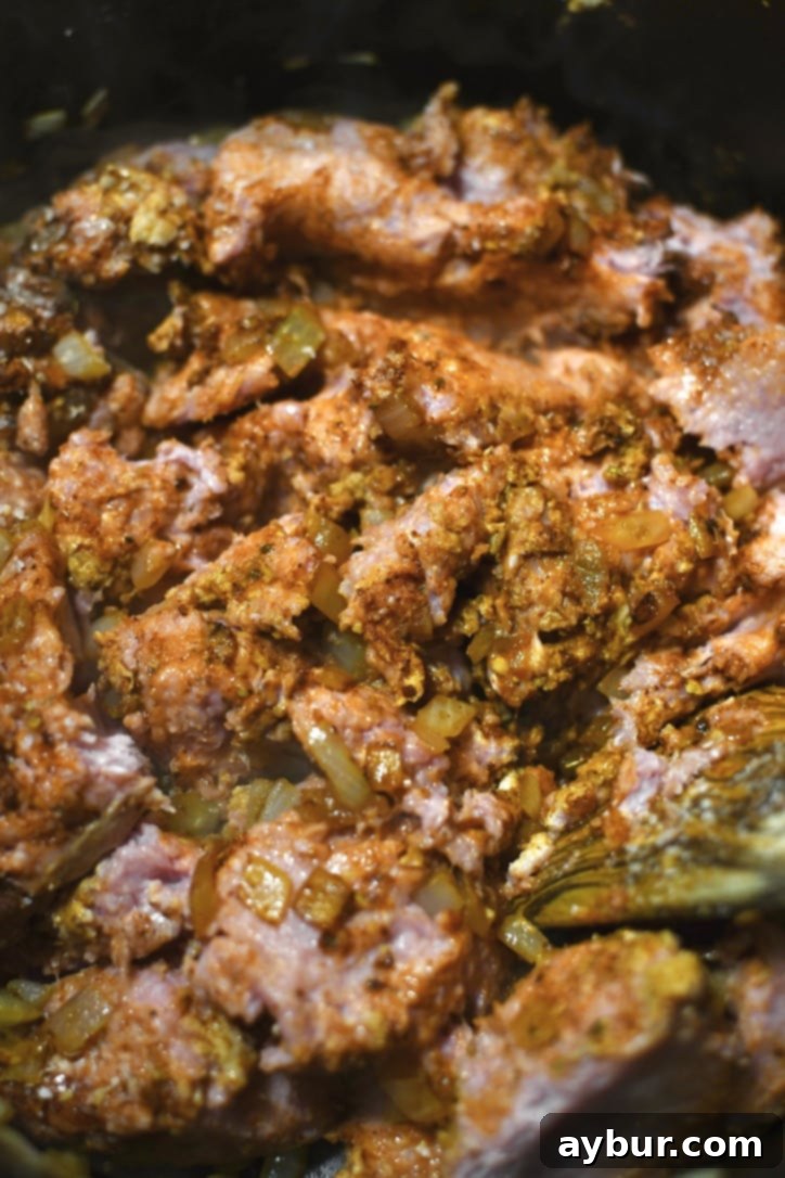 Breaking up raw ground turkey in a pot with a spatula as it cooks, mixing with seasonings.