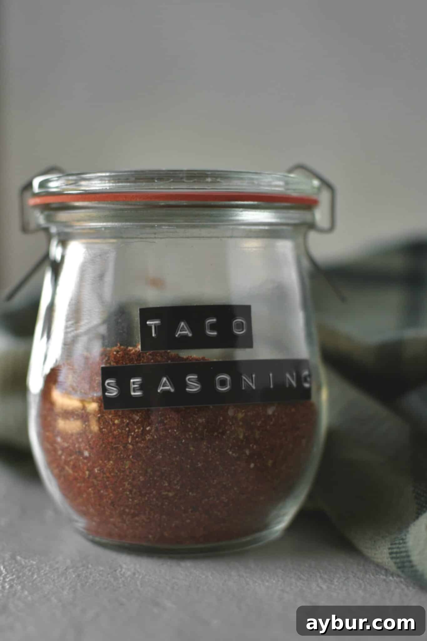 DIY Taco Spice Blend 6 A glass jar filled with homemade taco seasoning, positioned on a rustic wooden surface, with a small spoon next to it, indicating it's ready to be used or stored.