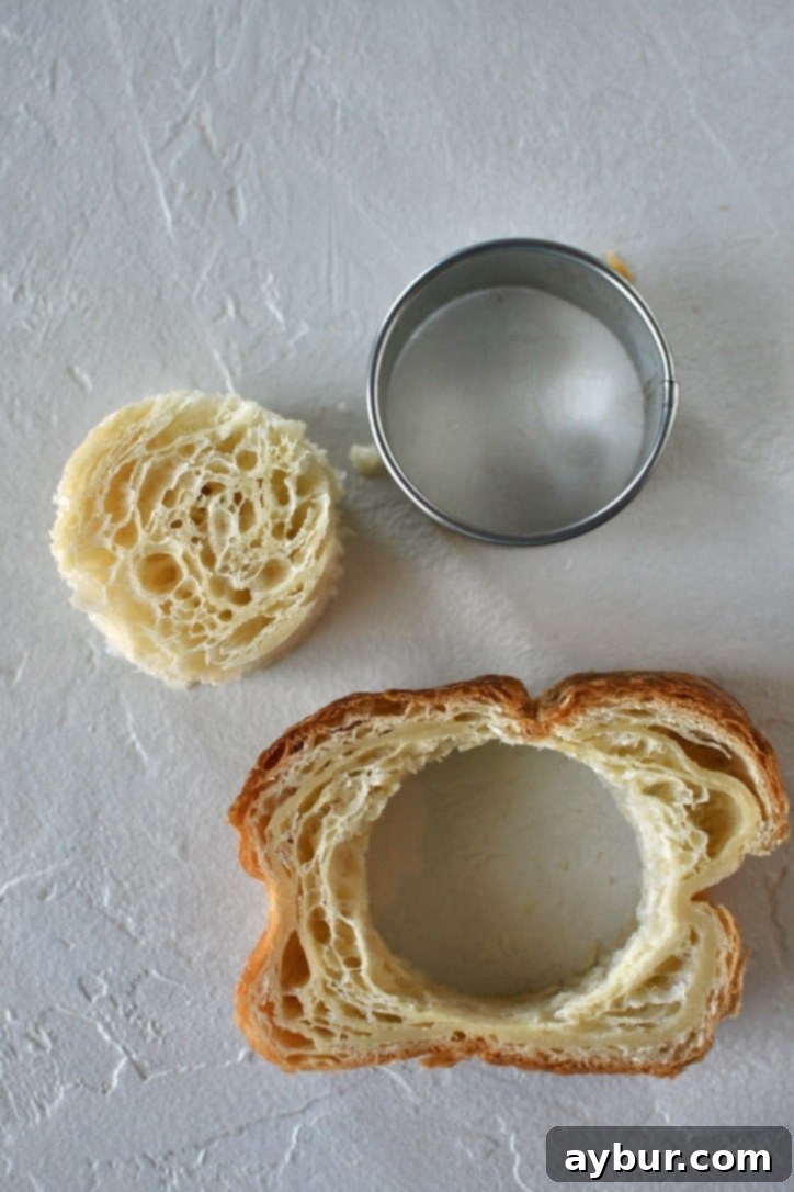 Croissant Toast on a work surface with a round cutter next to it and the center cut out of the bread.