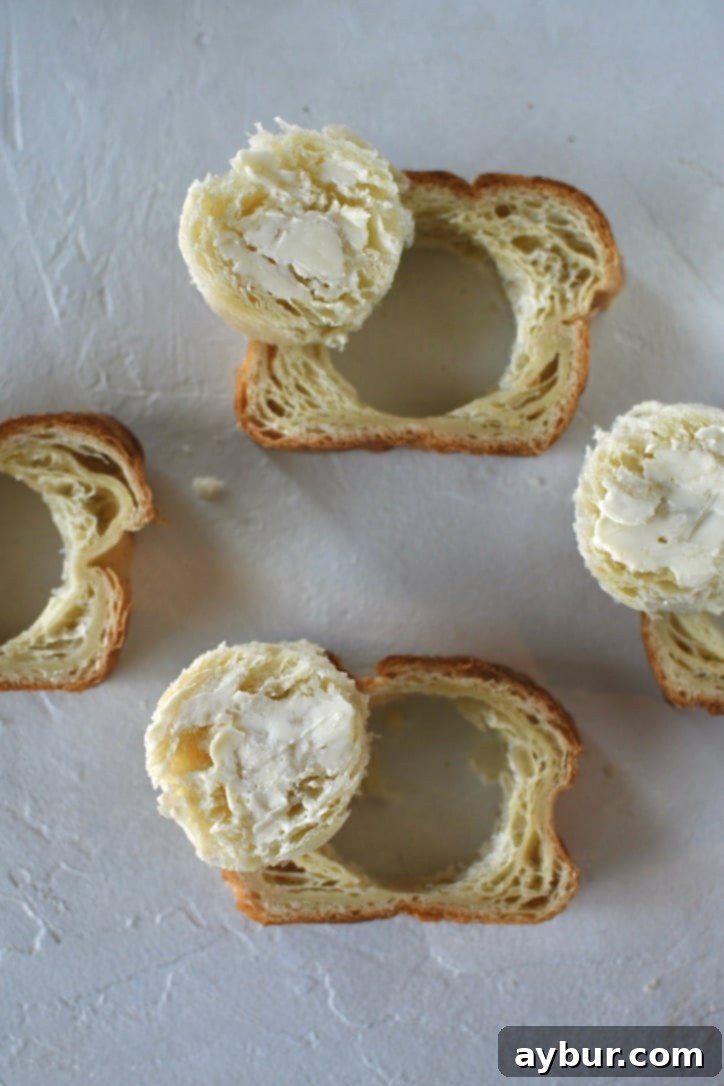 Four Croissant Toast slices on a work surface with the centers cut out and buttered on one side.