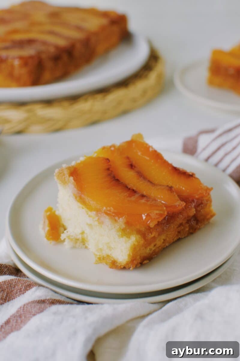 A beautifully presented slice of homemade Peach Upside-Down Cake on a white plate, showcasing the golden caramelized peaches and moist cake texture.
