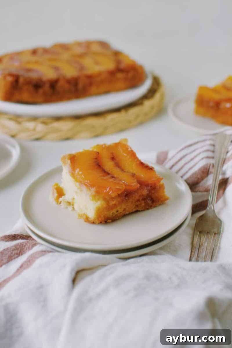 A beautifully presented slice of Peach Upside-Down Cake on a white plate, garnished with a mint leaf, highlighting its moist texture and vibrant colors.
