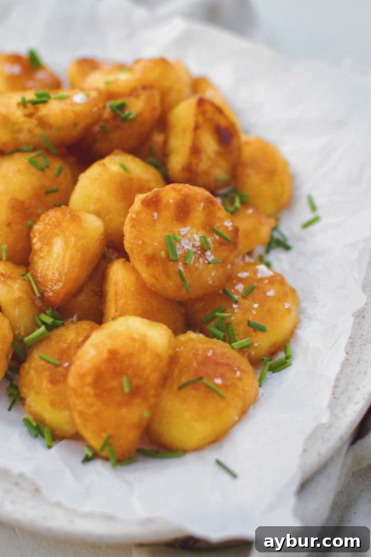 Addictively Crispy Roasted Potatoes 2 Crispy Roasted Potatoes on a platter topped with flakey sea salt and chopped chives, showcasing their golden-brown perfection.