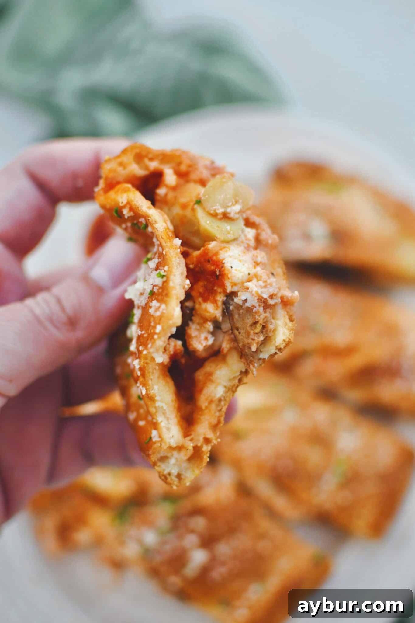 Holding a piece of calzone in hand with a bite taken out of it, showing all the gooey cheese and delicious fillings inside.