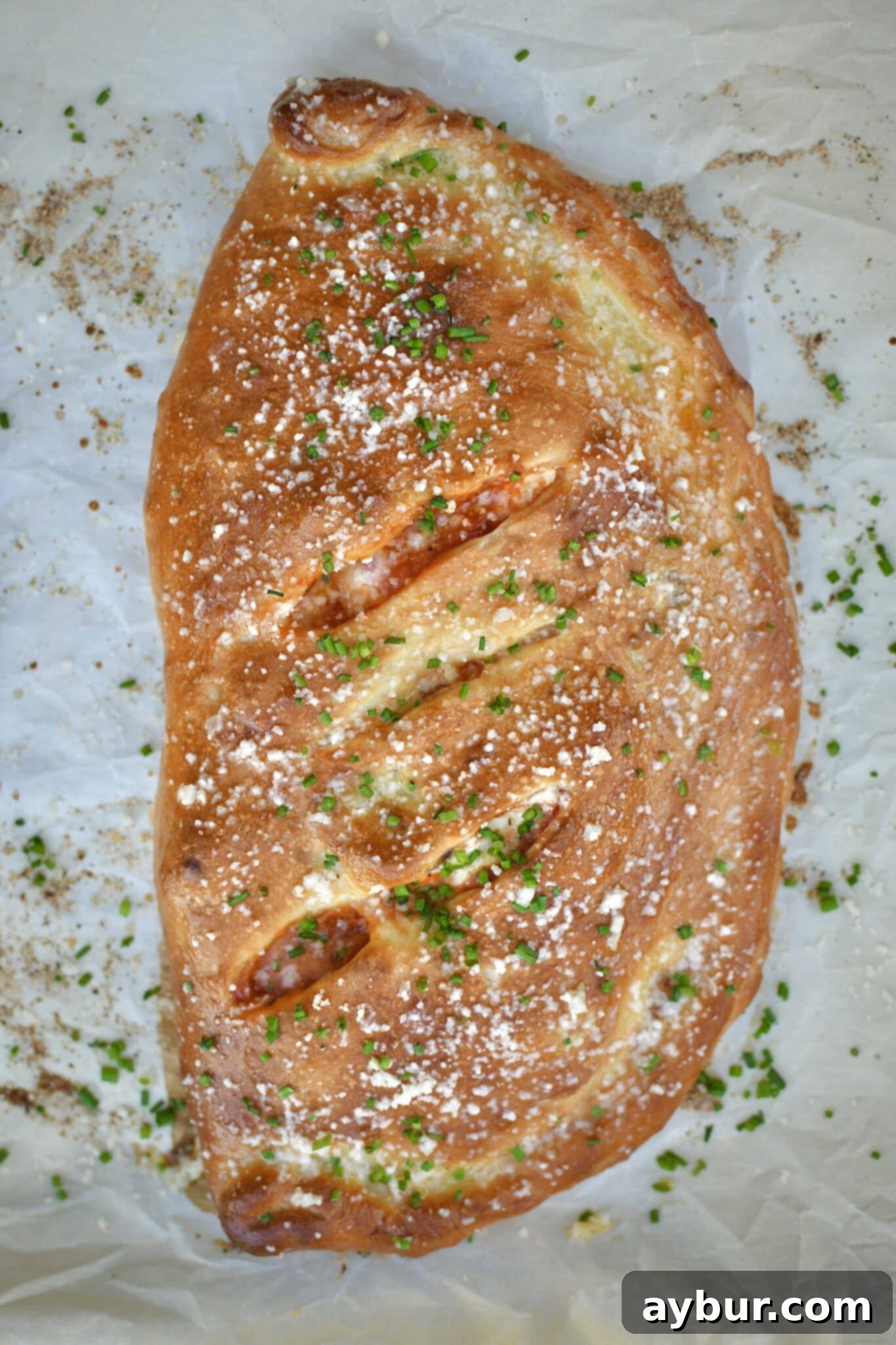 A freshly baked calzone, golden brown and glistening, brushed with garlic butter and dusted with grated parmesan and chives.