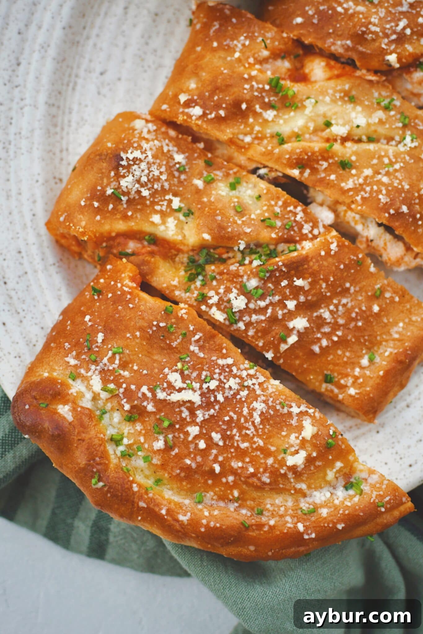 A perfectly baked calzone, sliced open to reveal its abundant fillings, brushed with garlic butter, and garnished with parmesan and chives. Served alongside a bowl of marinara dipping sauce.