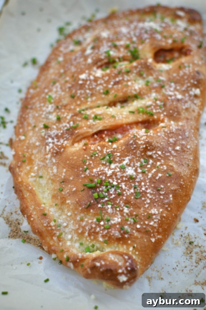A freshly baked calzone, glistening with garlic butter and dusted with grated parmesan and chives, ready to be served.