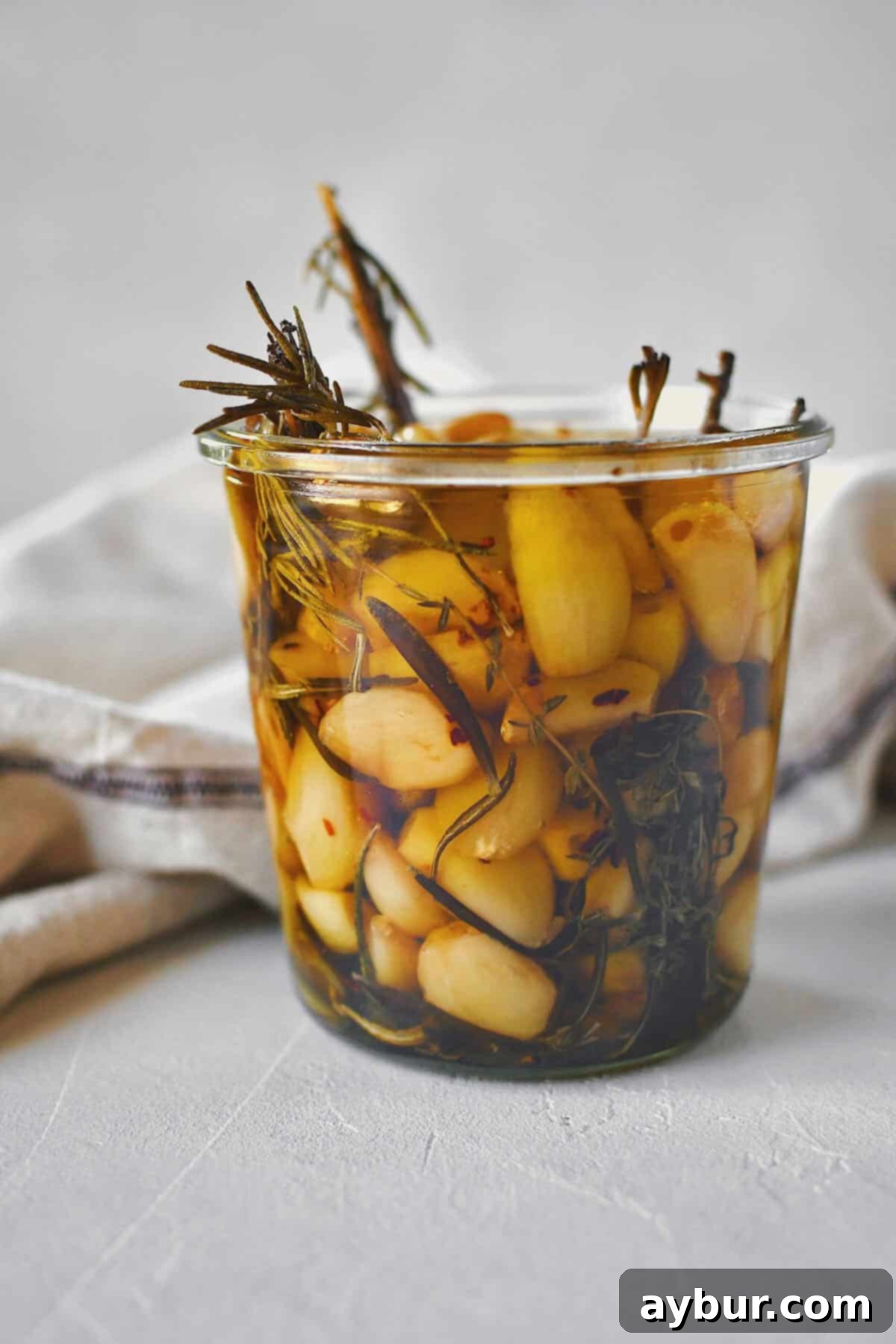 Velvety Garlic Confit 11 A close-up shot of a glass jar filled with confit garlic cloves submerged in golden olive oil.