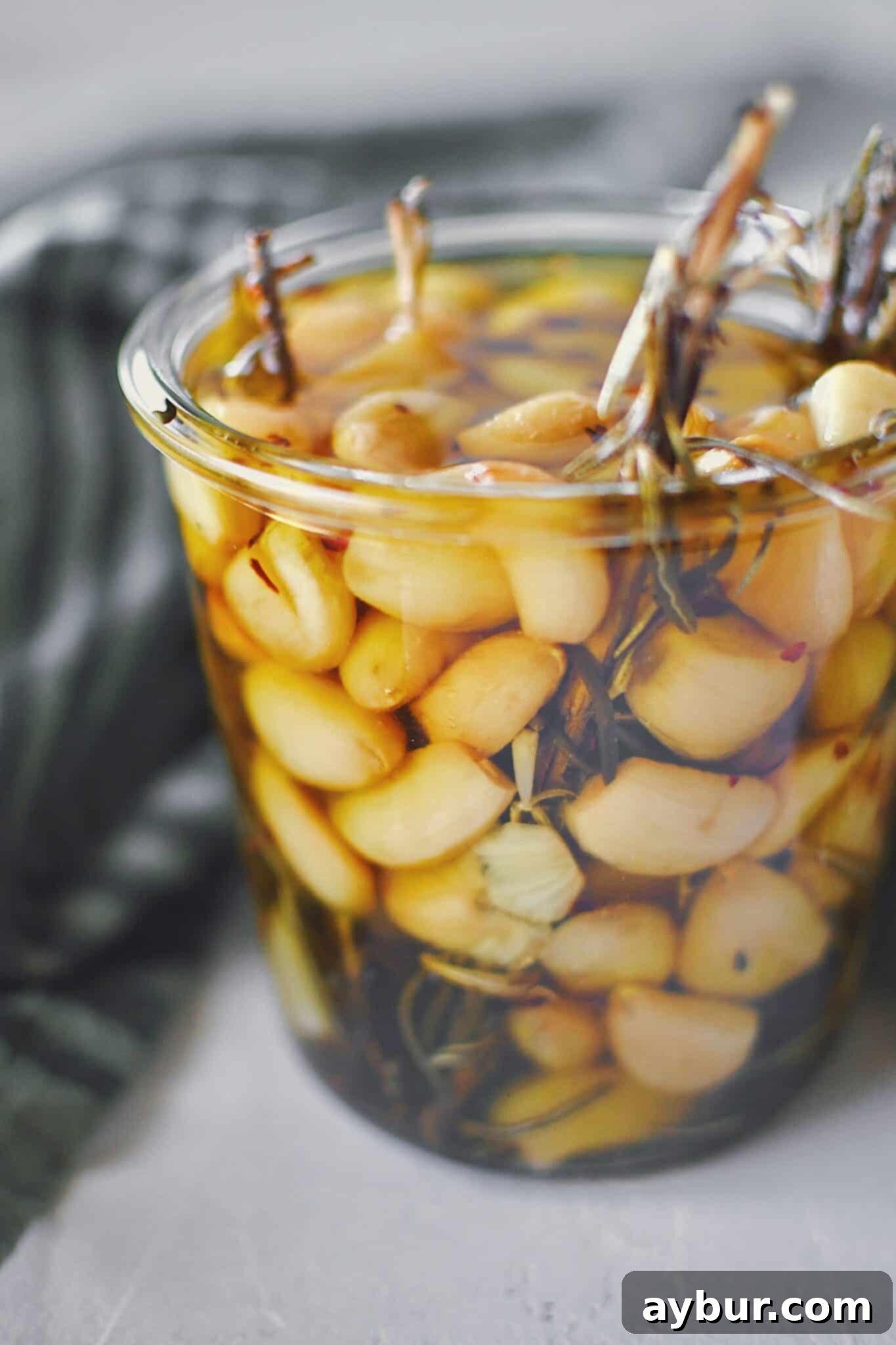 Velvety Garlic Confit 10 A glass jar of confit garlic and oil, with a clean spoon ready to scoop out the flavorful cloves.