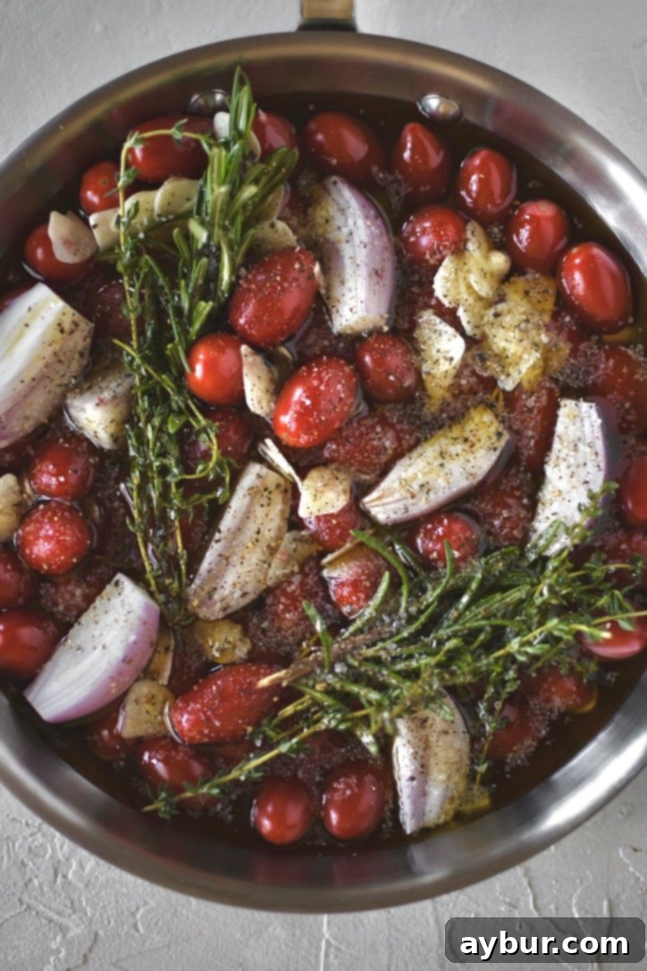 Slow-Roasted Tomato Confit 5 Grape tomatoes in a pan with shallots, sliced garlic, thyme, rosemary, salt, and pepper ready to be roasted and made into confit.