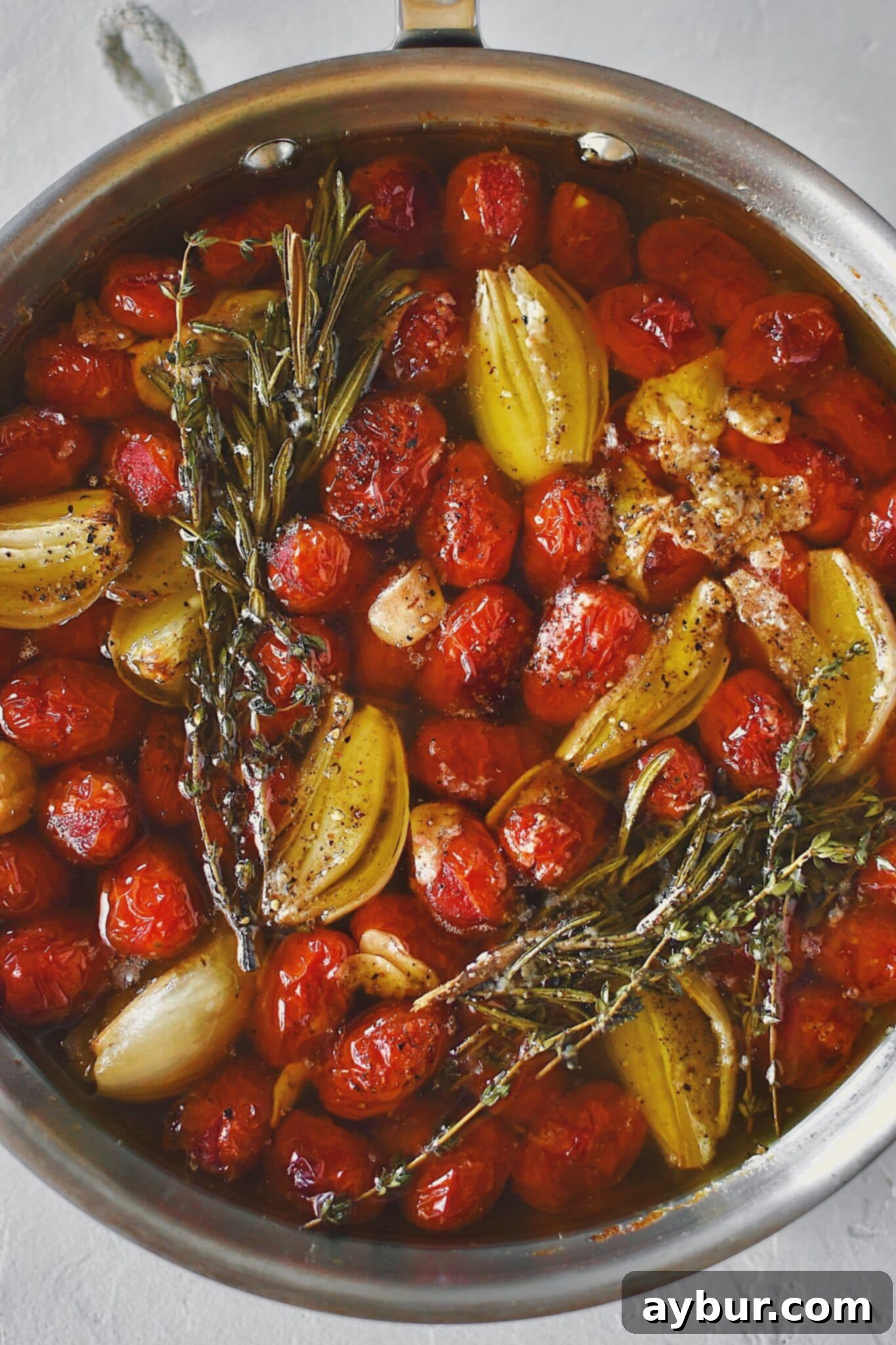 Slow-Roasted Tomato Confit 6 Grape tomatoes in a pan with shallots, sliced garlic, thyme, rosemary, salt, and pepper after roasting and made into confit.