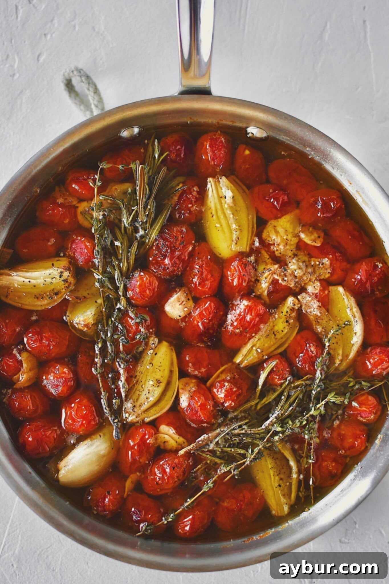 Slow-Roasted Tomato Confit 8 Grape tomatoes in a pan with shallots, sliced garlic, thyme, rosemary, salt, and pepper after roasting and made into confit.
