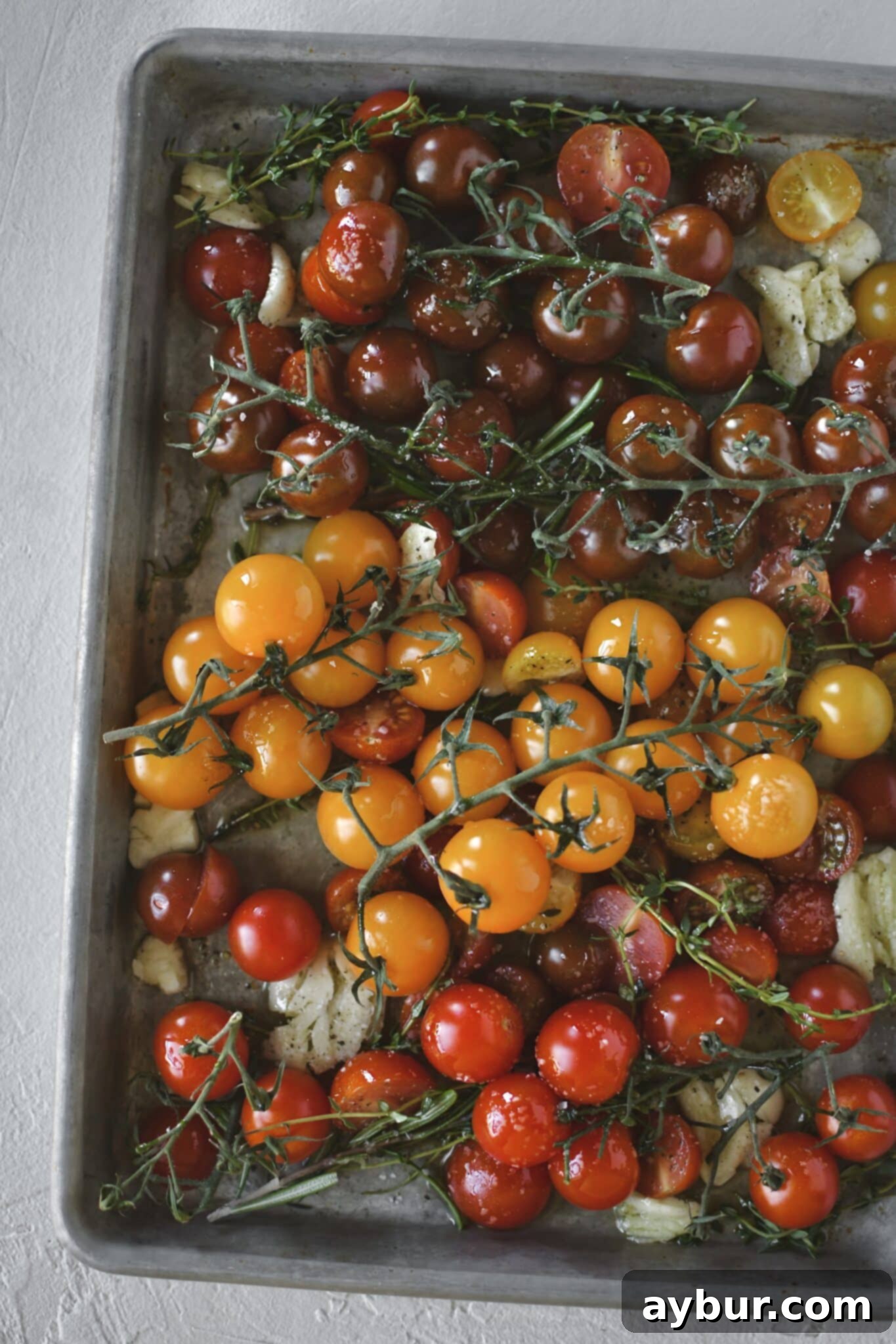 Sweet Roasted Cherry Tomatoes 5 Close-up of seasoned cherry tomatoes, garlic, and fresh herbs on a baking sheet, ready for the oven.