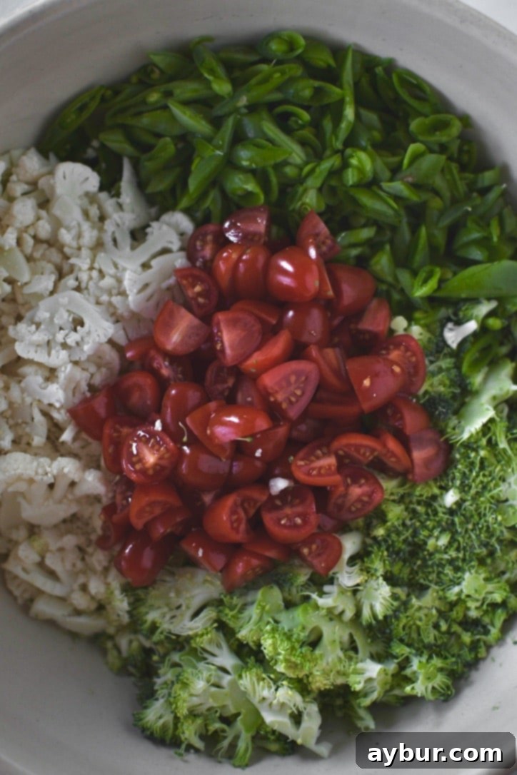 Crisp Snap Pea Salad 4 Finely sliced snap peas, broccoli, cauliflower, and quartered grape tomatoes prepped in a bowl, ready for dressing.