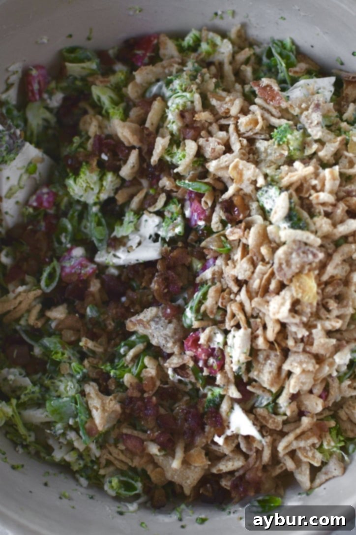 Crisp Snap Pea Salad 6 Snap pea salad being prepared, with finely chopped vegetables and dressing, as bacon bits and crispy onions are added to the bowl for mixing.