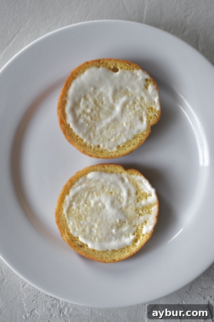 Applying a generous layer of creamy horseradish sauce to the inside of a freshly toasted brioche bun, preparing it for the other delicious fillings.