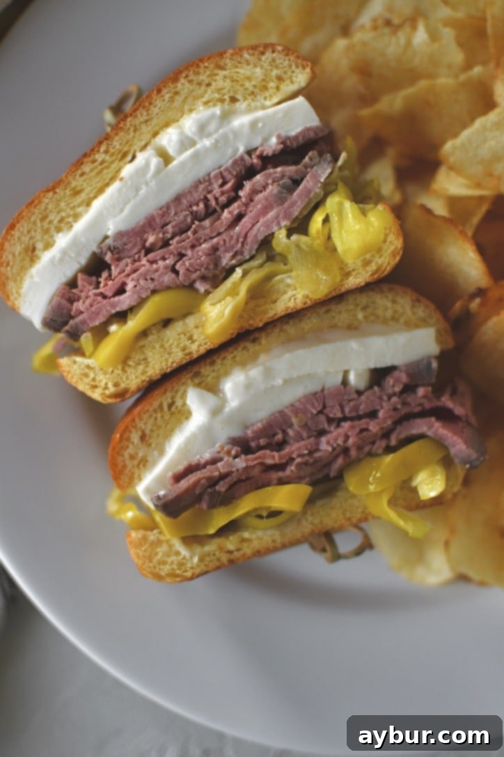 A delicious roast beef sandwich, expertly cut in half to showcase its flavorful layers, served on a plate with potato chips on the side, ready to be enjoyed as a meal.