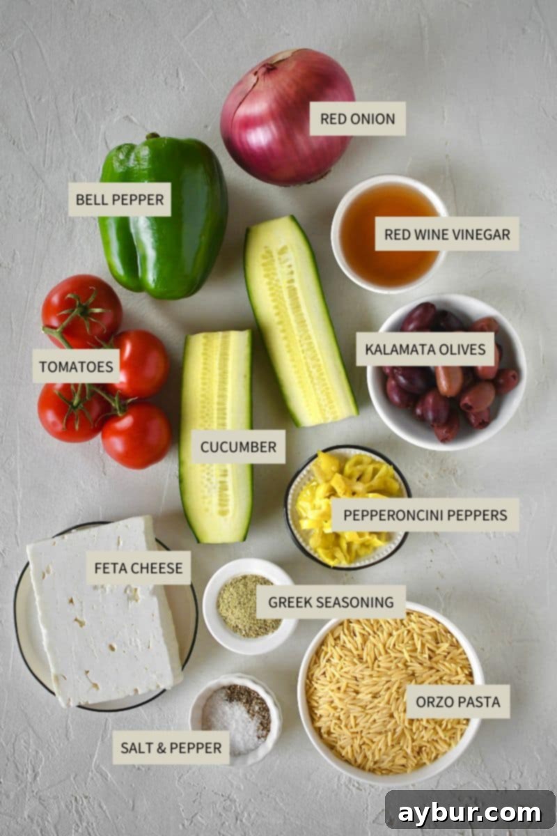Various fresh ingredients laid out on a kitchen counter, including bell peppers, cucumbers, red onion, tomatoes, orzo pasta, kalamata olives, feta cheese, and olive oil, ready for making Greek Pasta Salad.