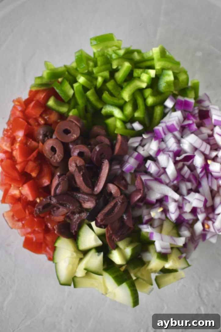 Chopped vegetables, including cucumbers, bell peppers, tomatoes, and red onions, being added to a large mixing bowl along with kalamata olives.