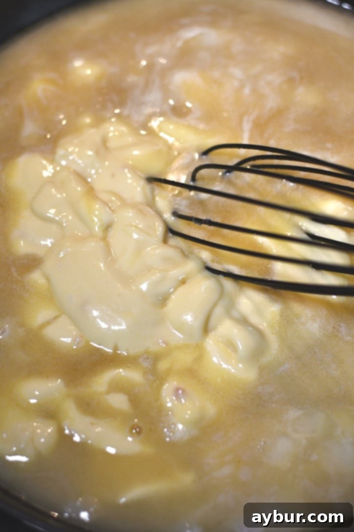 Gradually whisking chicken stock into the roux to create the savory sauce base for the filling.