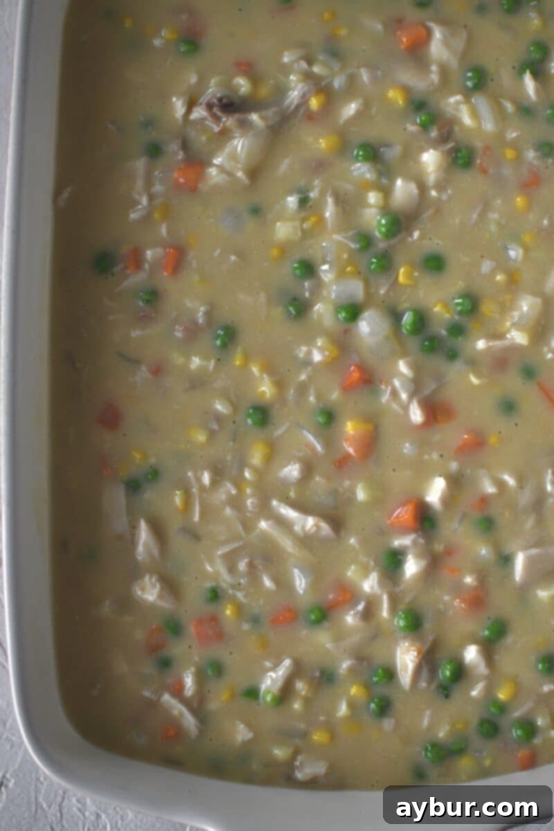 Dolloping individual portions of cheesy biscuit dough onto the chicken filling, preparing for baking.