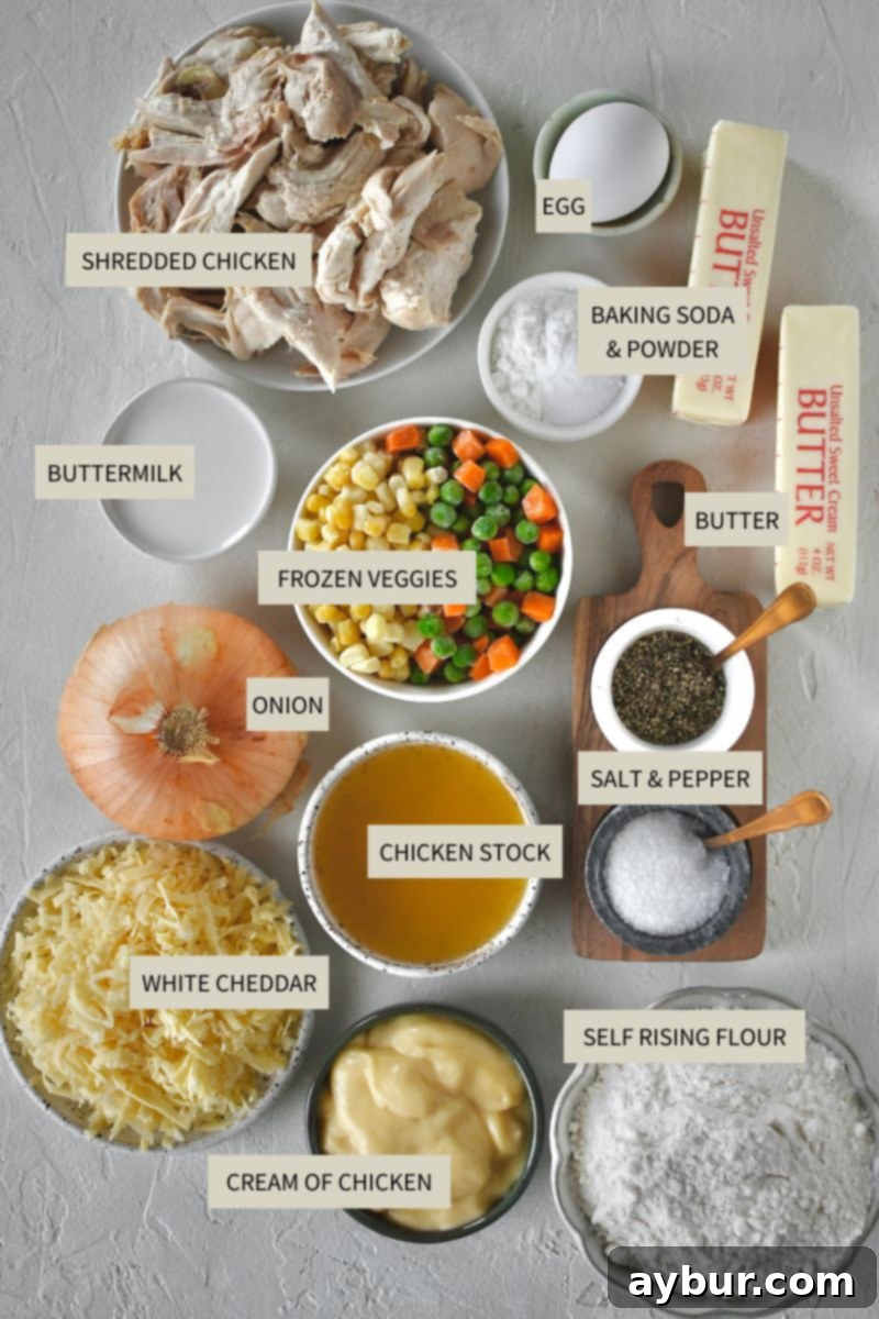 A complete array of fresh and pantry ingredients laid out for making Chicken and Biscuits, including shredded chicken, mixed vegetables, butter, and white cheddar cheese.