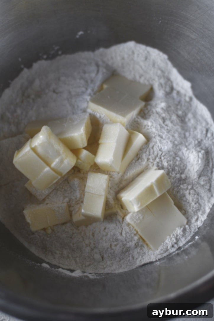 Image showing room temperature butter being cut into the flour mixture for the cheesy biscuit topping, forming pea-sized pieces.