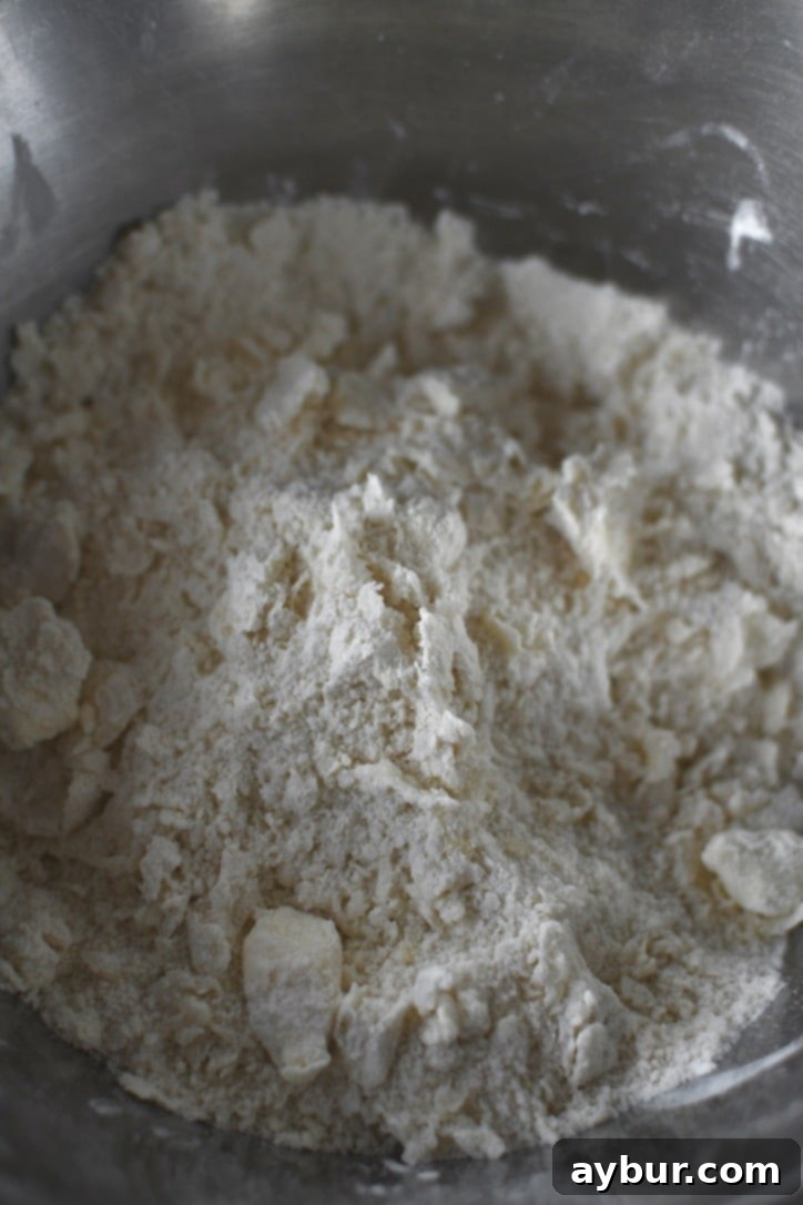 Adding buttermilk and egg mixture to the flour and butter, ready to be mixed into a sticky biscuit dough.