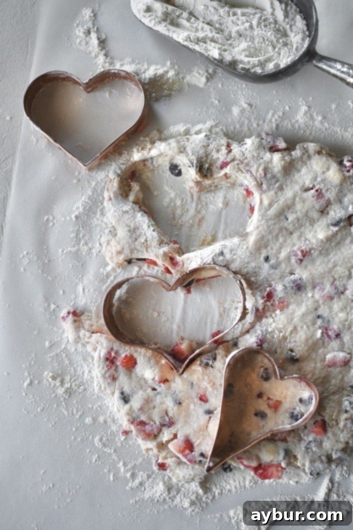 Heart shapes being carefully cut from the flattened scone dough using a cookie cutter.
