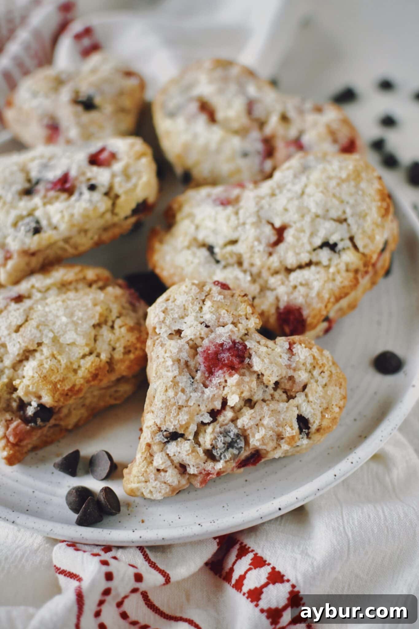 A close-up of a heart-shaped Strawberry Scone on a white plate, highlighting its golden crust and topping.