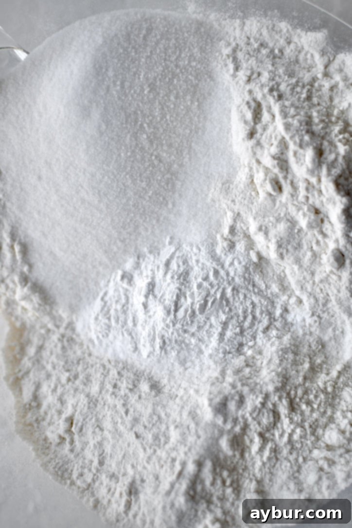 Dry ingredients like flour, sugar, baking powder, baking soda, and salt are ready in a mixer bowl.