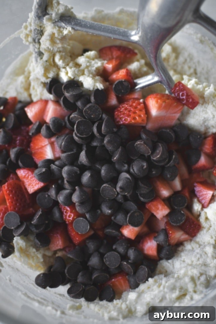 Freshly diced strawberries and chocolate chips being added to the shaggy scone dough in a mixer.