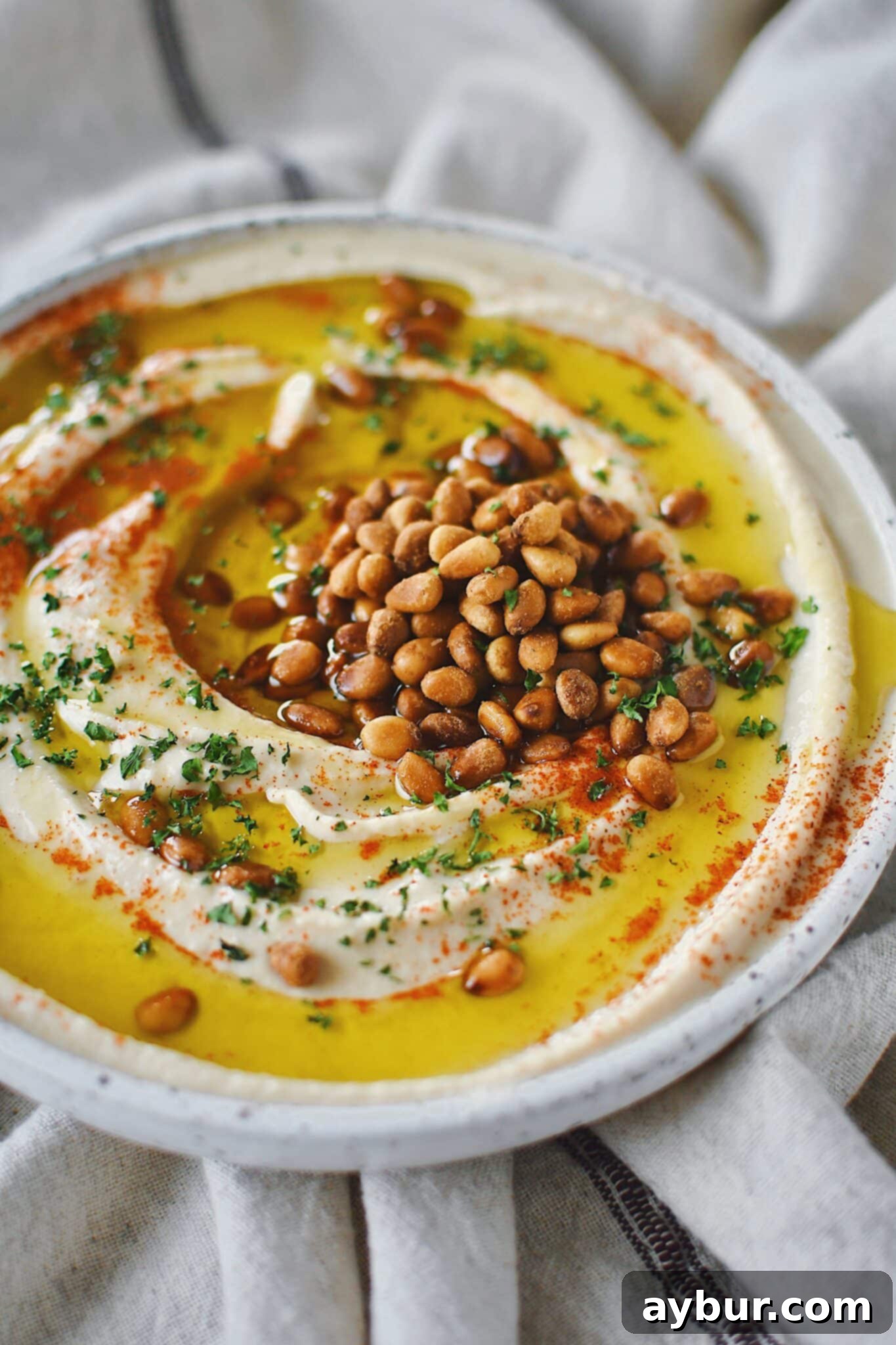 Creamy Homemade Hummus Perfection 2 Homemade Hummus, topped with olive oil, paprika, toasted pine nuts, and parsley, ready to eat.