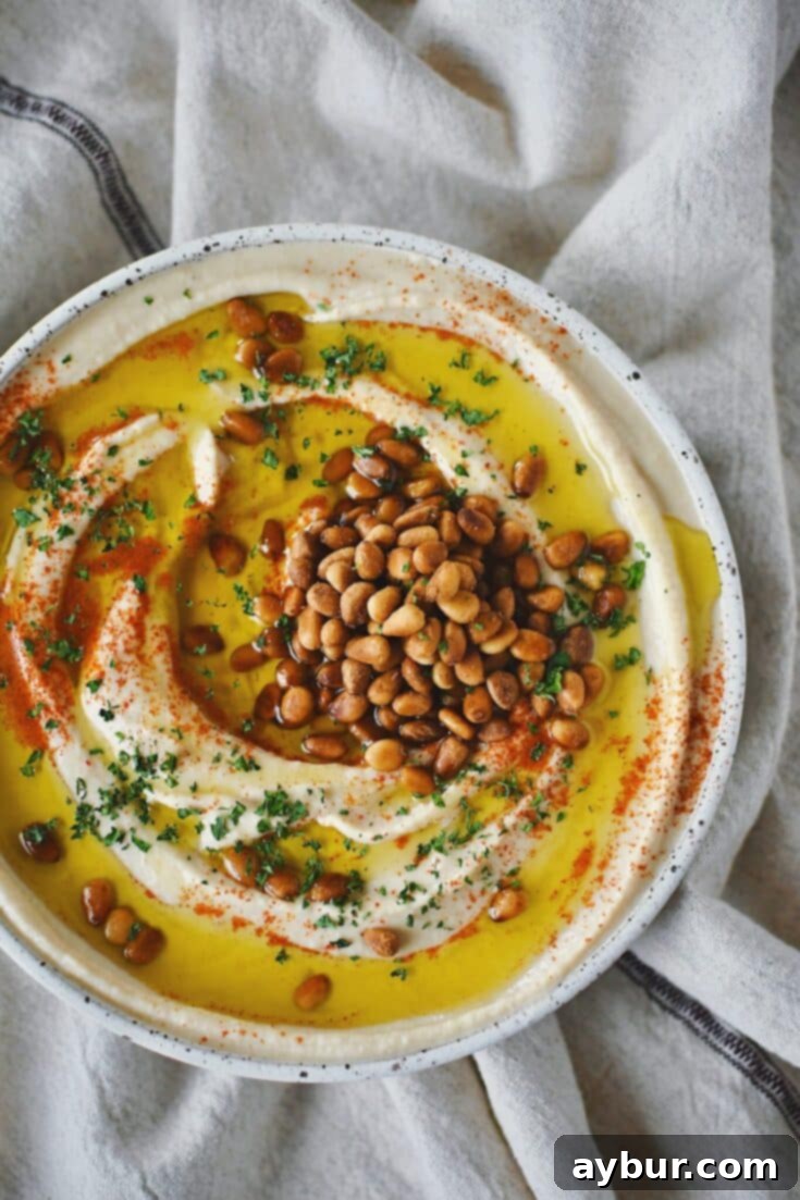 Creamy Homemade Hummus Perfection 11 Homemade Hummus, topped with olive oil, paprika, toasted pine nuts, and parsley, ready to eat.