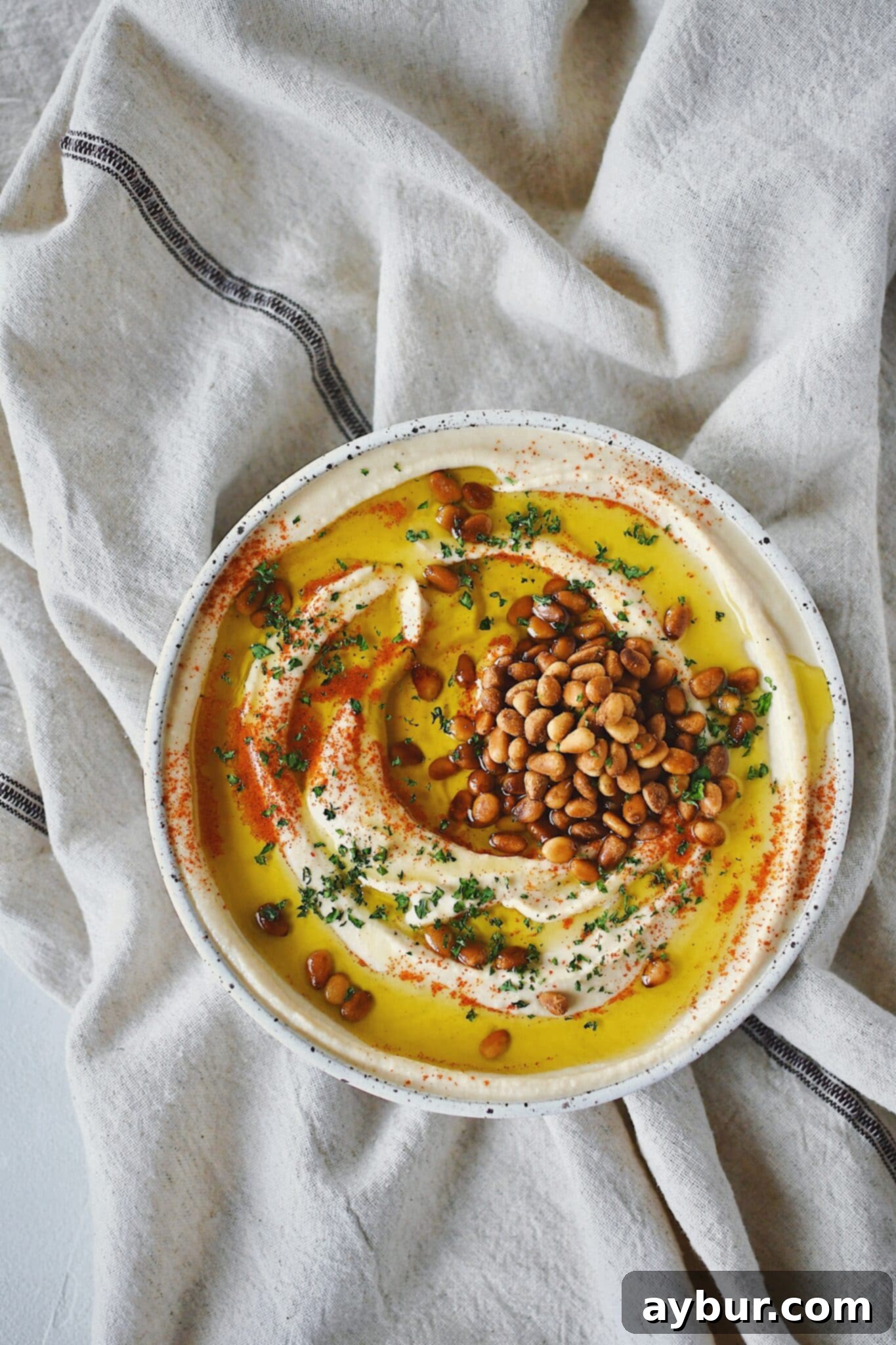 Creamy Homemade Hummus Perfection 12 Homemade Hummus, topped with olive oil, paprika, toasted pine nuts, and parsley, ready to eat.