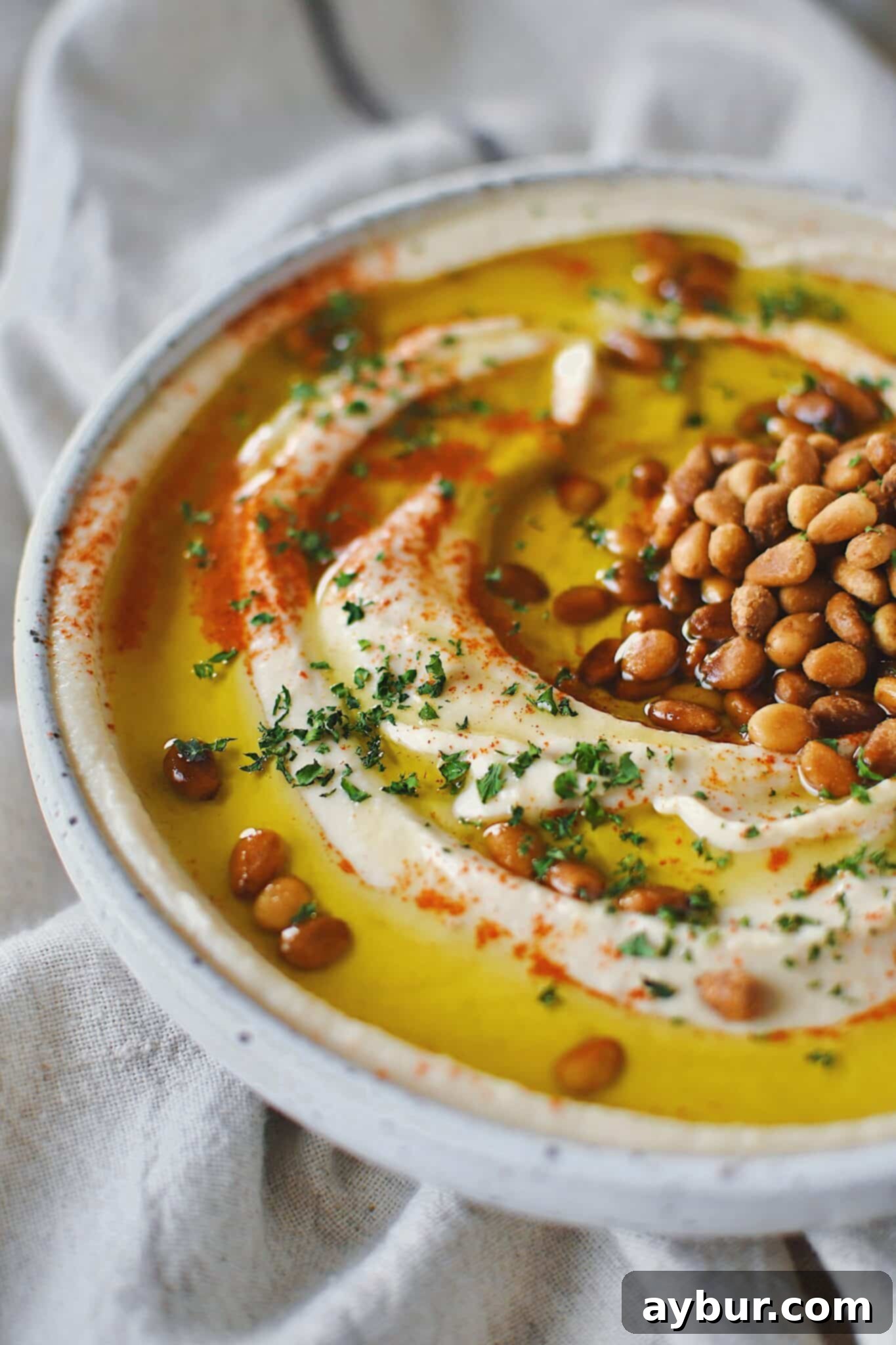 Creamy Homemade Hummus Perfection 10 Homemade Hummus, topped with olive oil, paprika, toasted pine nuts, and parsley, ready to eat.
