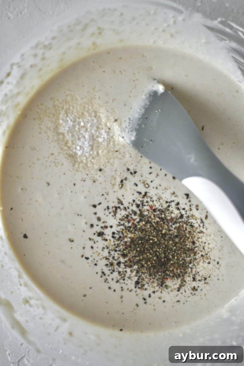 The horseradish cream sauce has been perfectly stirred, with a sprinkle of salt and pepper visible on its surface, awaiting final seasoning adjustments.