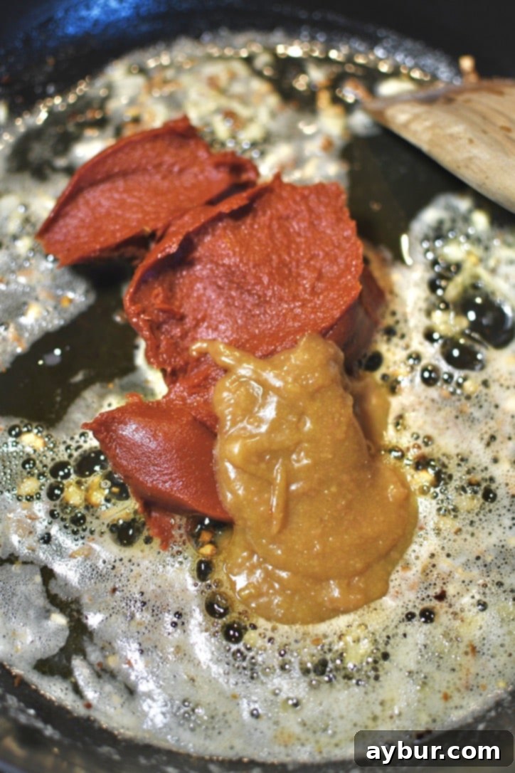 Adding the tomato paste and chicken bouillon paste to the browned garlic and chili flakes in the pan.