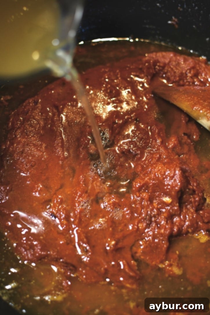 Adding the chicken stock and water to the pastes to form the base of the sauce.