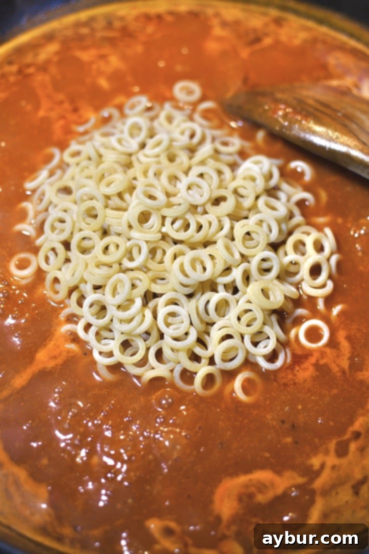 Placing the Anelletti pasta in the pan with the simmering sauce.