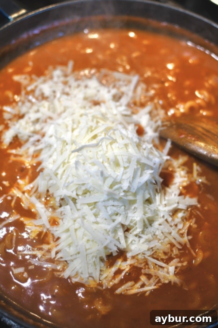 Adding cheese to cooked pasta and sauce in the pan, stirring to melt.