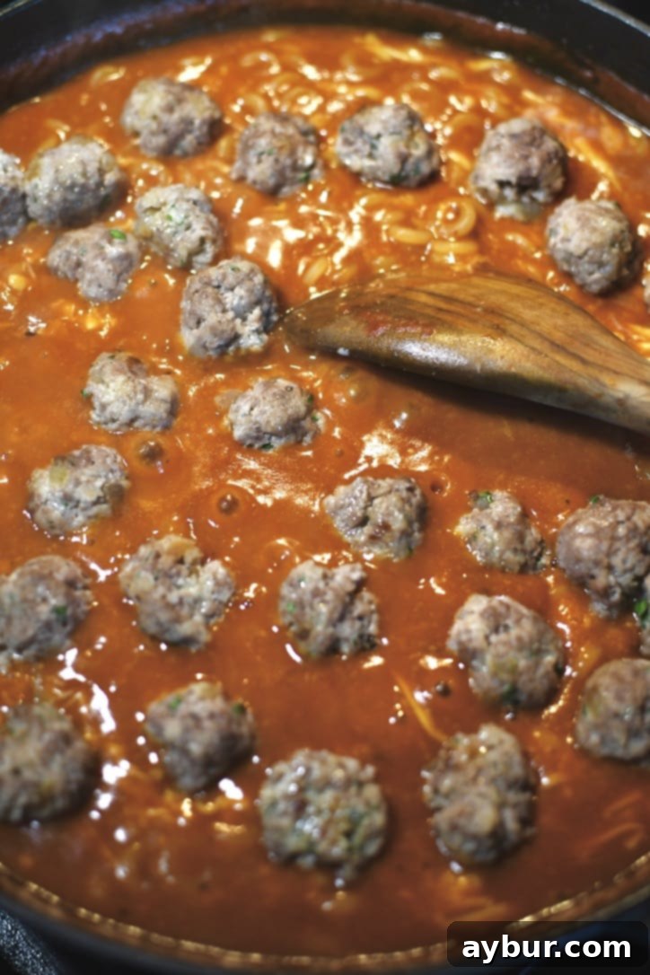 Gently placing the cooked tiny meatballs into the pan with the pasta and sauce.