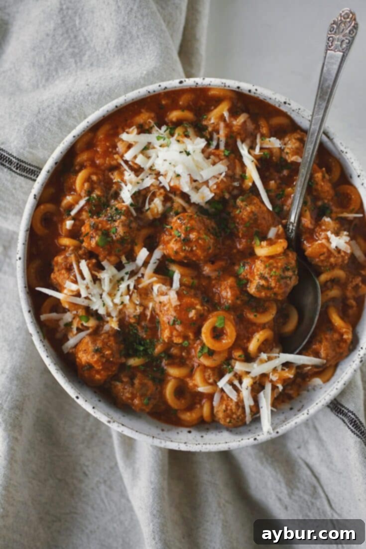 Homemade Spaghettios with meatballs in a bowl with a spoon topped with extra cheese and parsley.