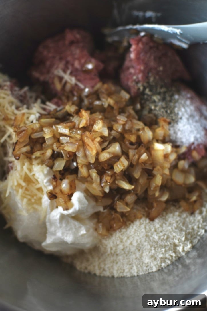 Ground beef and dry ingredients for meatballs in a bowl after adding the cooked onions, ready to be mixed.