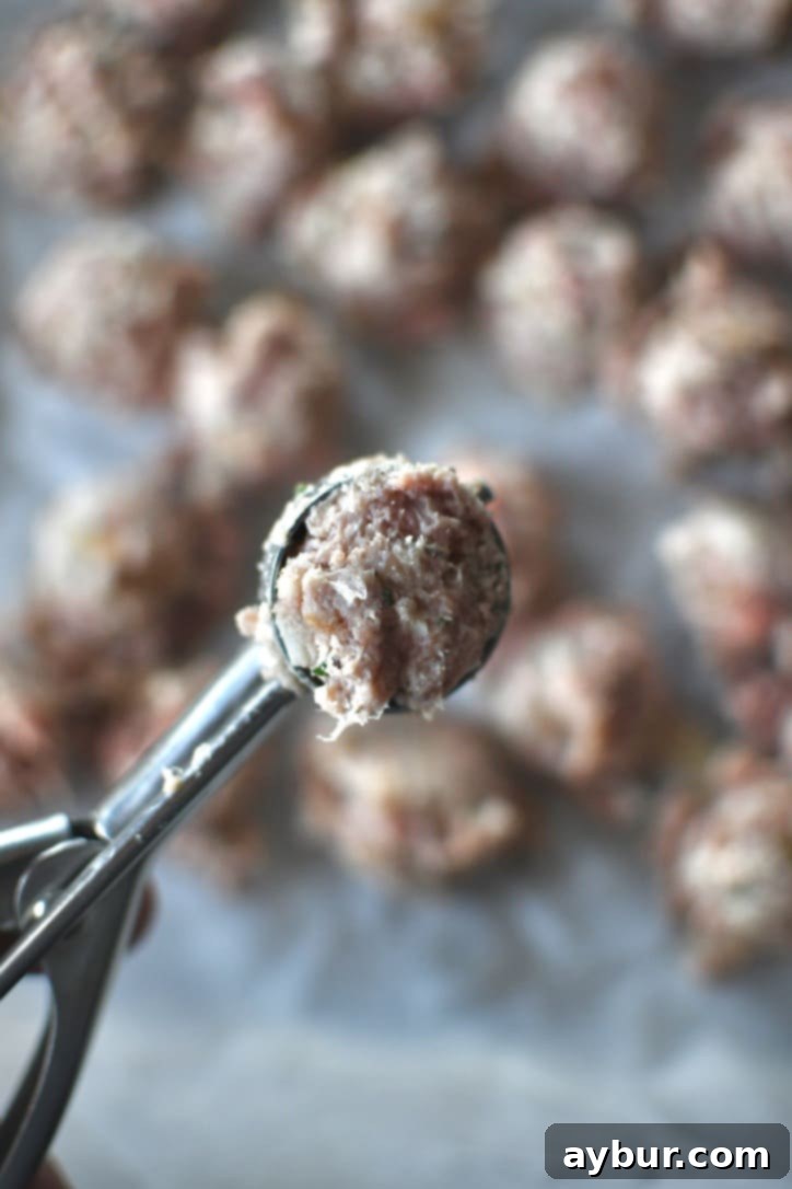 Portioning out the meatball mixture into tiny meatballs using a small scoop.