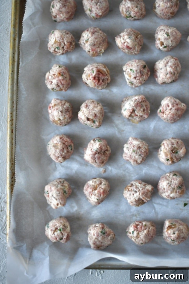 Portioned out meatball mixture into tiny meatballs, on a tray and meticulously rolled into uniform balls.