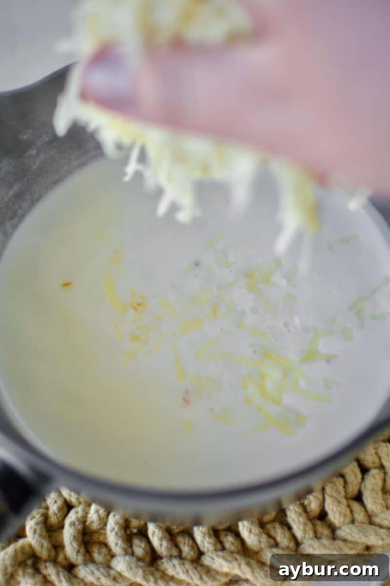 Creamy White Queso 5 Finely diced white American cheese and grated pepper jack cheese are added to the simmering milk and roux mixture in a pot, ready to be melted into a smooth dip.